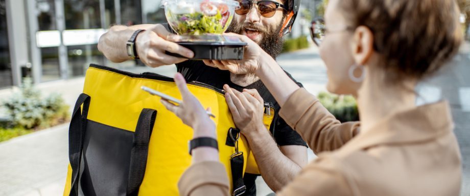 Courier delivering fresh lunches to a young business woman on a bicycle with thermal backpack. Takeaway restaurant food delivery concept